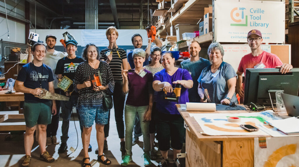 Lineup of Cville Tool Library volunteers posing with tools in the library